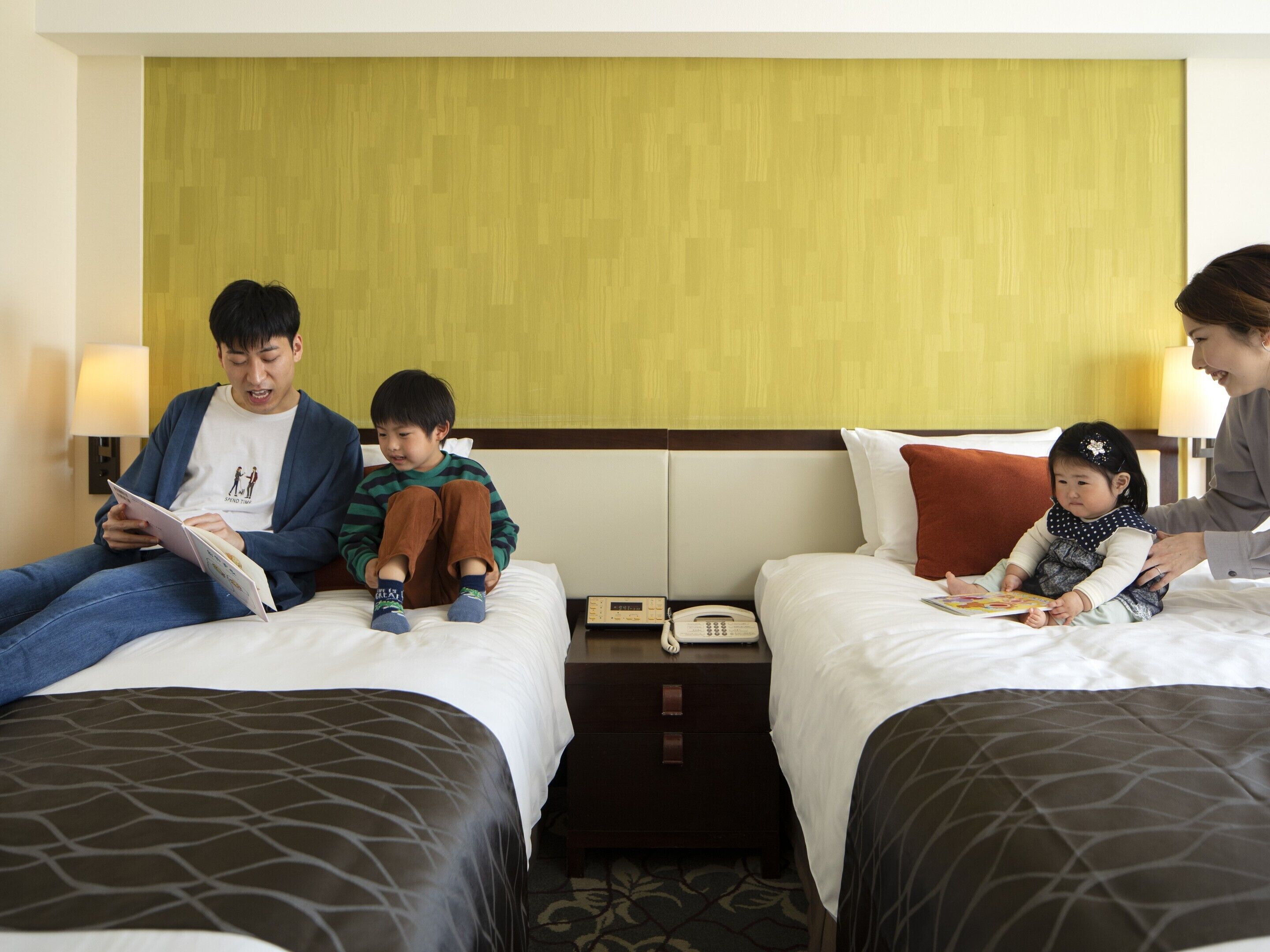 A hotel room with two beds, a nightstand with a phone, and a wall with a textured panel.