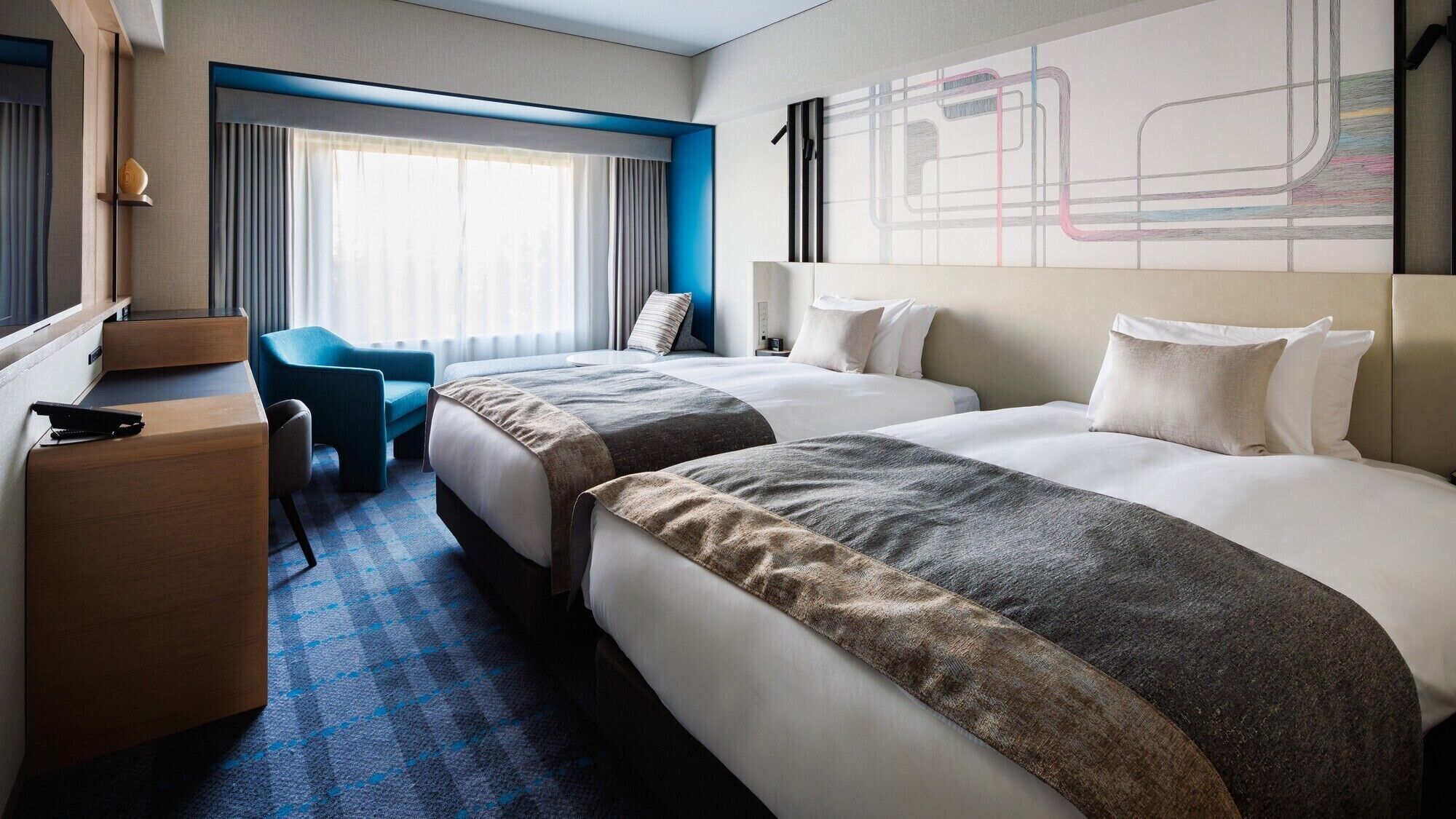 A hotel room with two beds, a desk, a chair, and a large abstract painting on the wall.