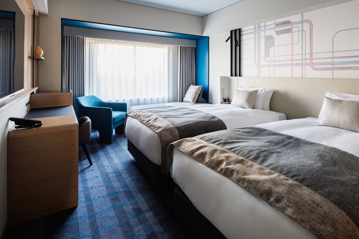 A hotel room with two beds, a desk, a chair, and a large abstract painting on the wall.