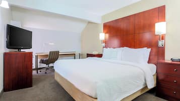 A hotel room with a large bed, a desk with a chair, a television, and a wooden headboard.