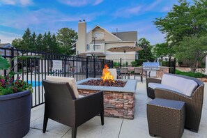 An outdoor patio with a fire pit, wicker furniture, and a pool in the background. - Residence Inn By Marriott Chicago Deerfield (Deerfield)