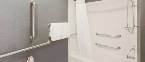 A modern bathroom with a bathtub, grab bars, a showerhead, and a towel rack.
