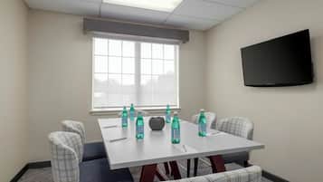 A conference room with a white table, four chairs, and a flat-screen TV mounted on the wall.