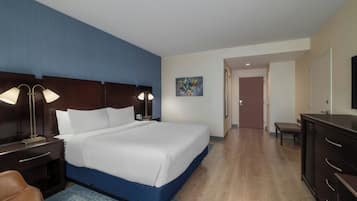 Habitación de hotel con una cama grande, lámparas de noche, un escritorio con silla, una mesita y un cuadro en la pared.