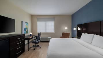 Una habitación de hotel con cama, escritorio, silla, televisión y una obra de arte en la pared.