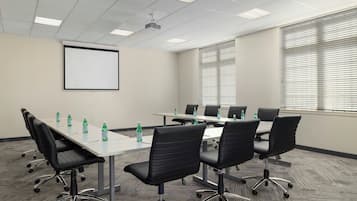 Une salle de conférence équipée d’un projecteur, d’un tableau blanc et d’une table avec des chaises.