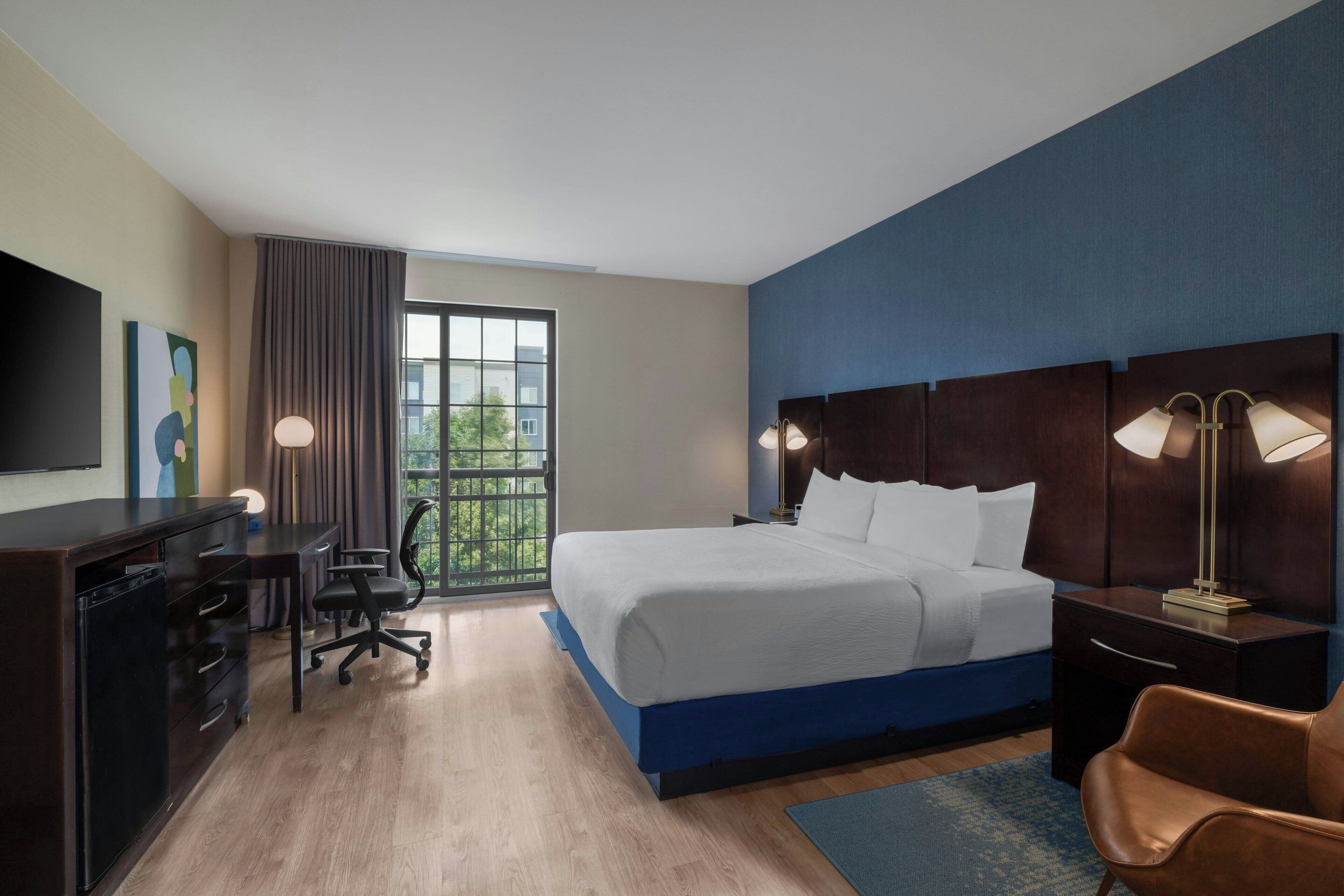 A hotel room with a bed, desk, chair, and a television.
