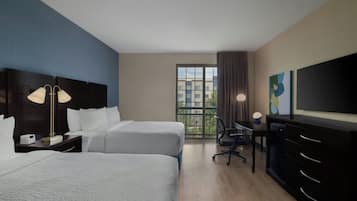 A hotel room with two beds, a desk, a chair, a TV, and a window with a view of buildings.