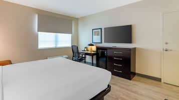 A hotel room with a bed, desk, chair, and a television.