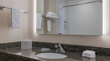 Un baño con encimera de granito, un lavabo, un espejo y un perchero con toallas dobladas.