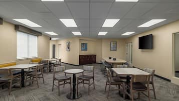 A conference room with multiple tables and chairs, a large window, and a flat-screen TV on the wall.