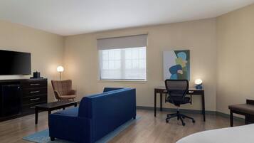 A hotel room with a sofa, a desk with a chair, a television, and a painting on the wall.