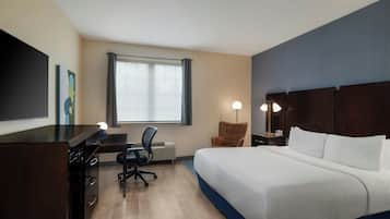 Ein Hotelzimmer mit Bett, Schreibtisch, Stuhl, Fernseher und einem Fenster mit Vorhängen.