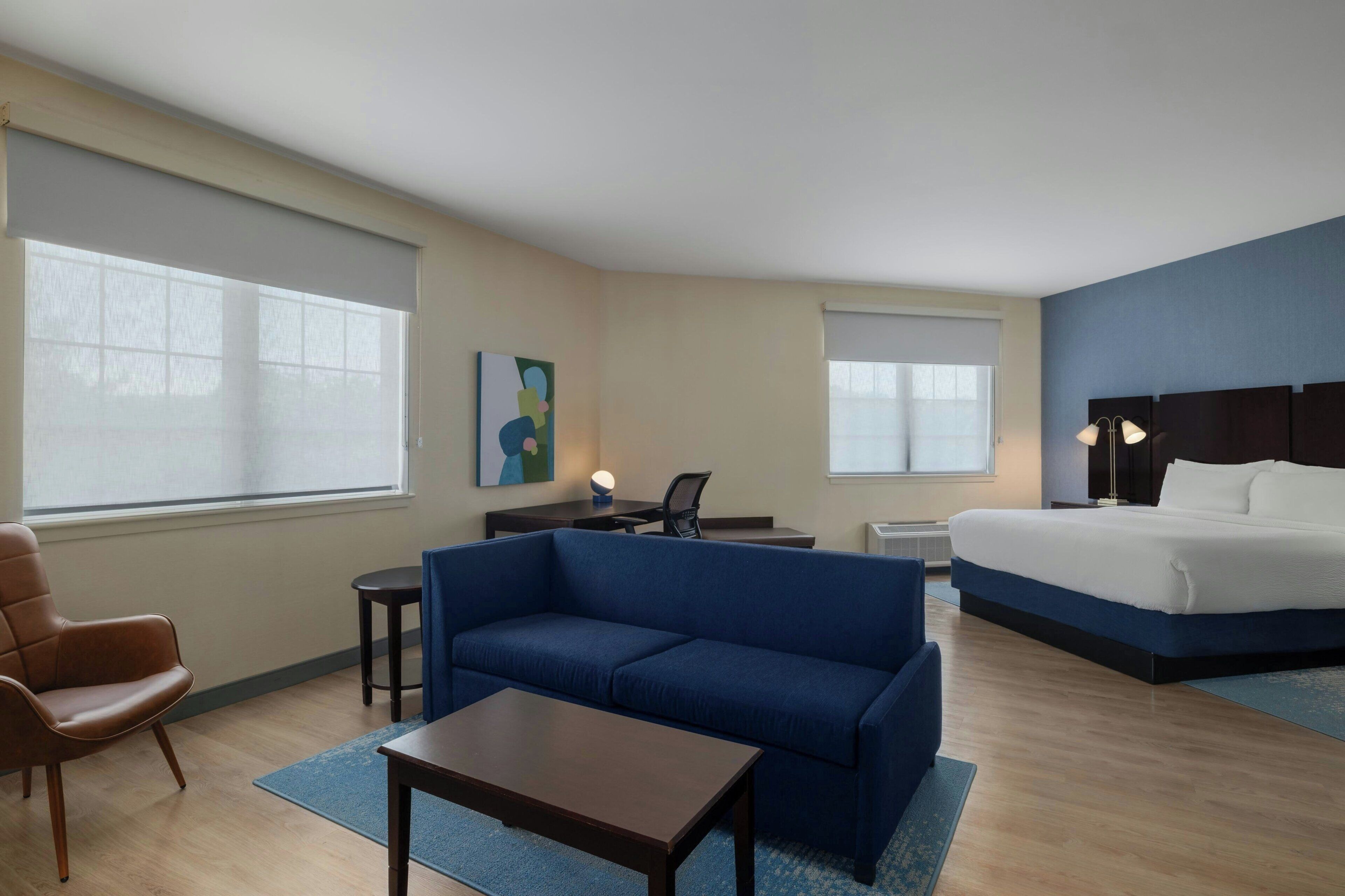 Une chambre d’hôtel avec un lit, un canapé, un bureau, une chaise et un tableau au mur.