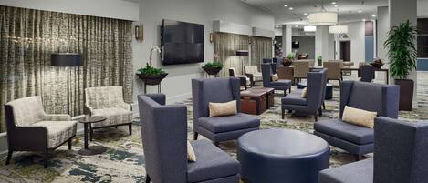 A spacious lobby with multiple seating areas, a large TV screen, and a patterned carpet.