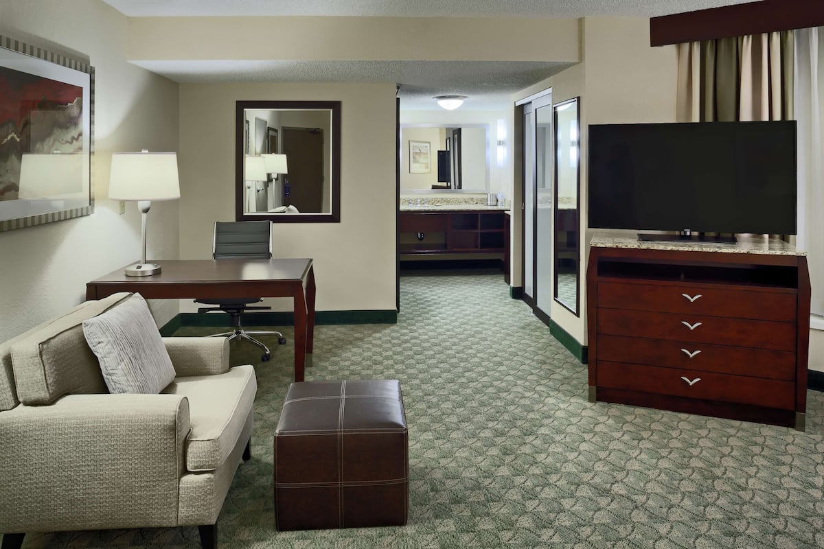 A hotel room with a sofa, a desk, a TV, a dresser, and a mirror.