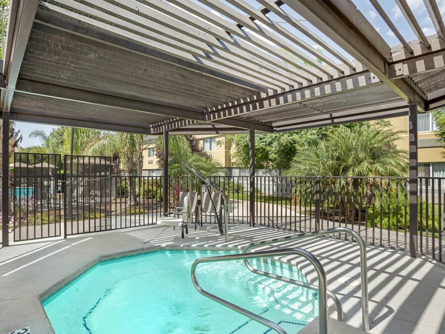 A covered outdoor swimming pool with a metal railing, a ladder, and a shaded area with a pergola.