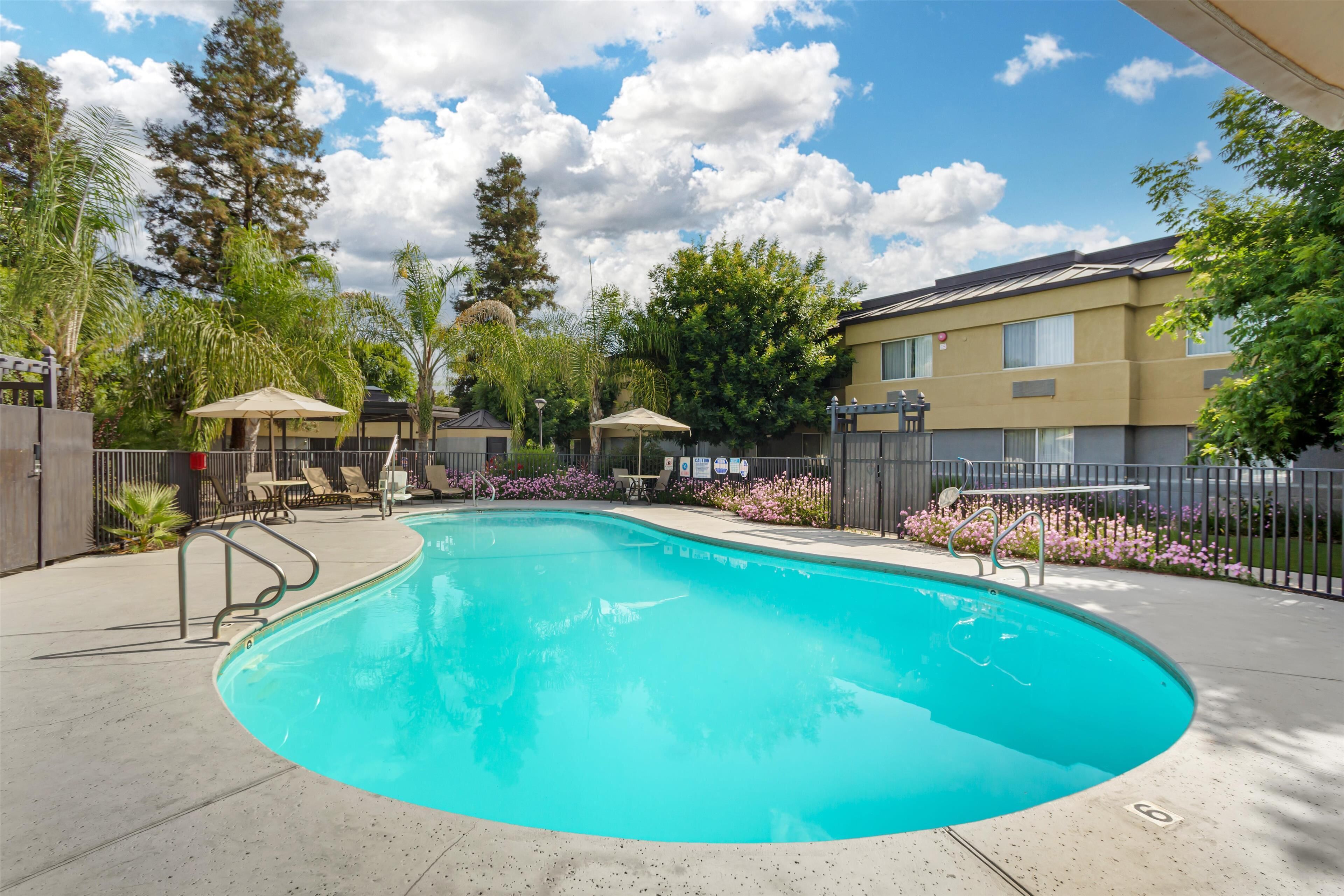 A swimming pool with lounge chairs and umbrellas, surrounded by a fence and trees.