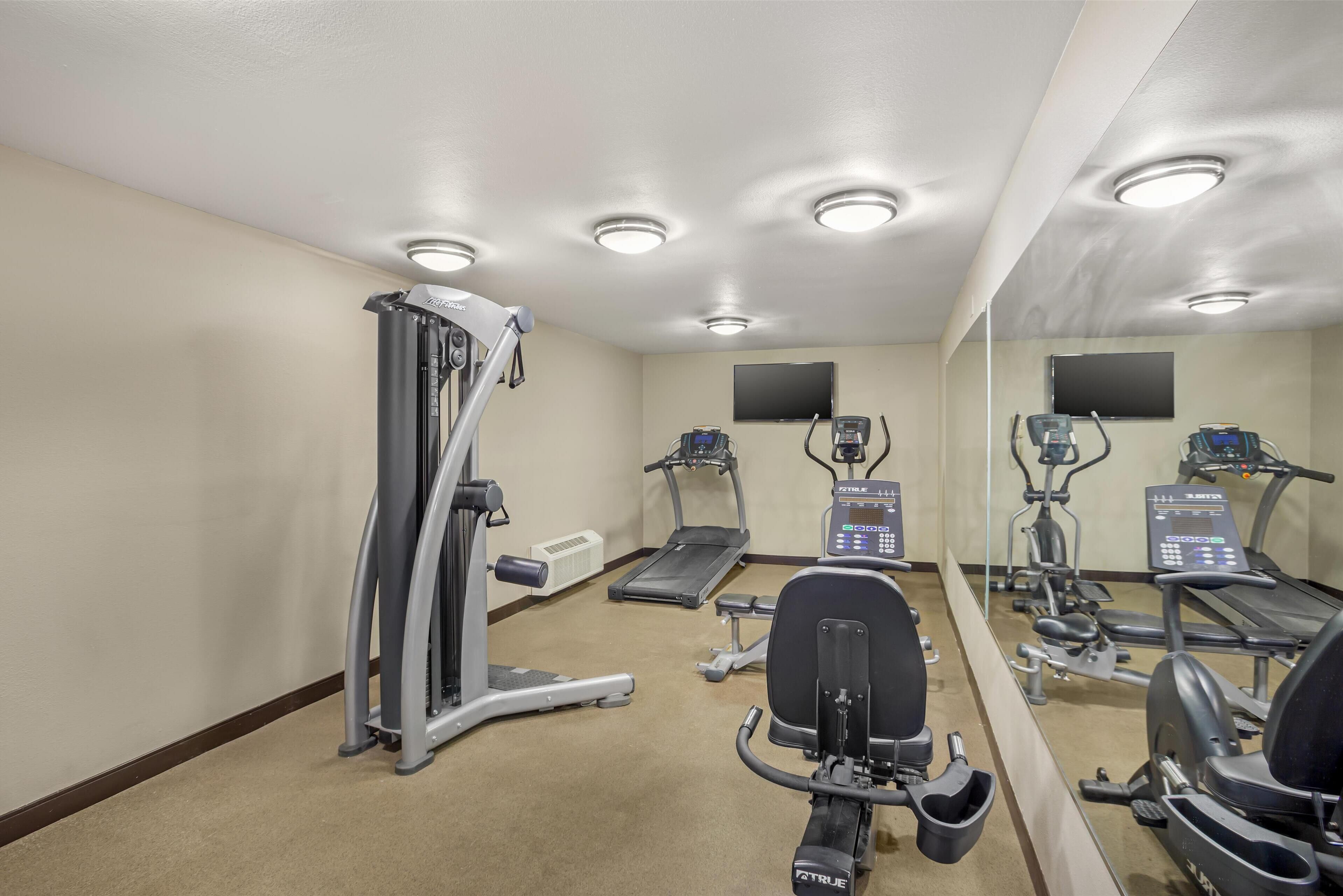 Un gimnasio con máquinas de cardio, una cinta de correr y un espejo grande.