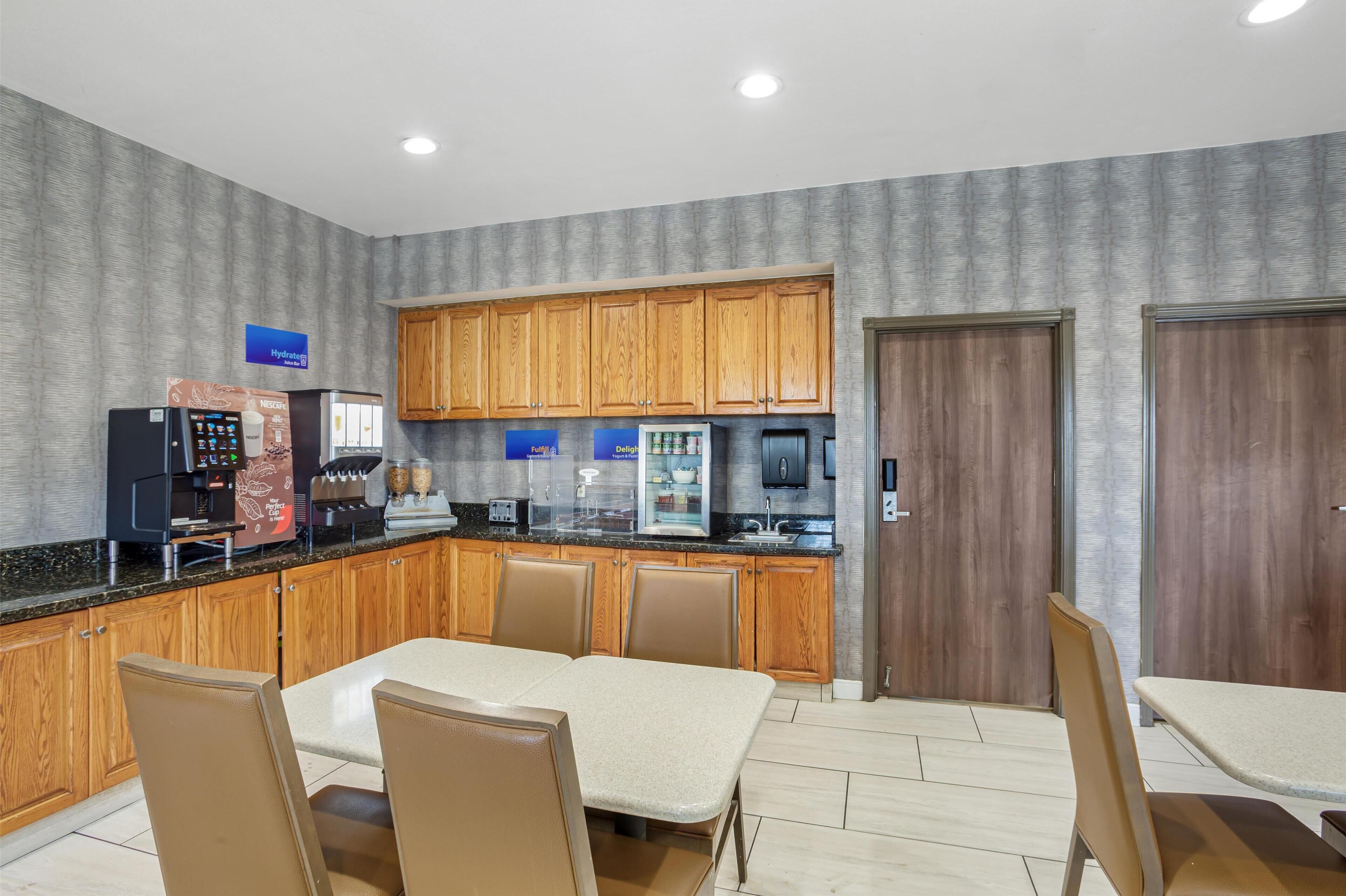 A modern kitchen with wooden cabinets, a coffee machine, and a refrigerator. There is a dining area with a table and chairs.