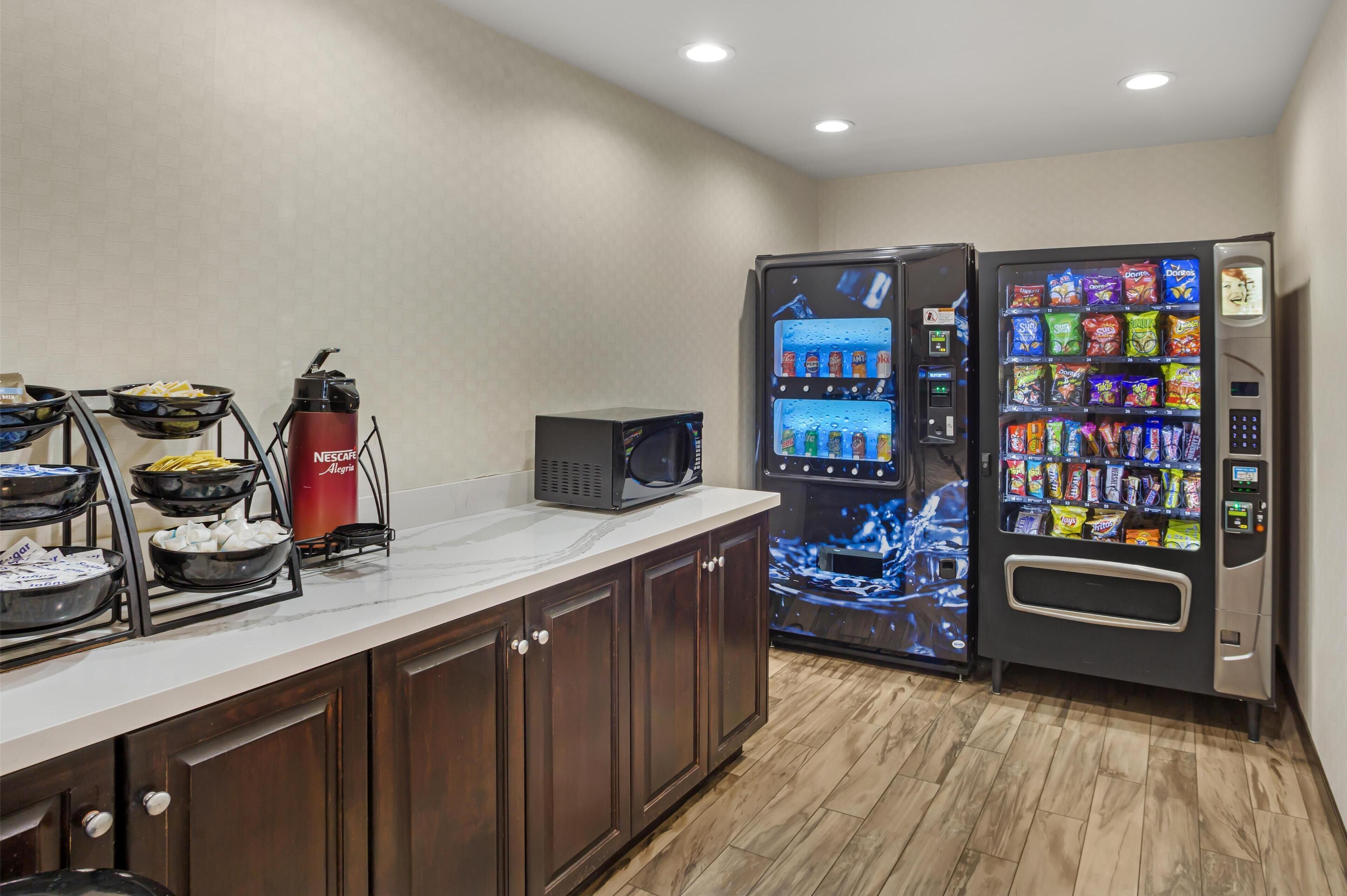 A kitchen area with a microwave, a beverage dispenser, and a snack vending machine.