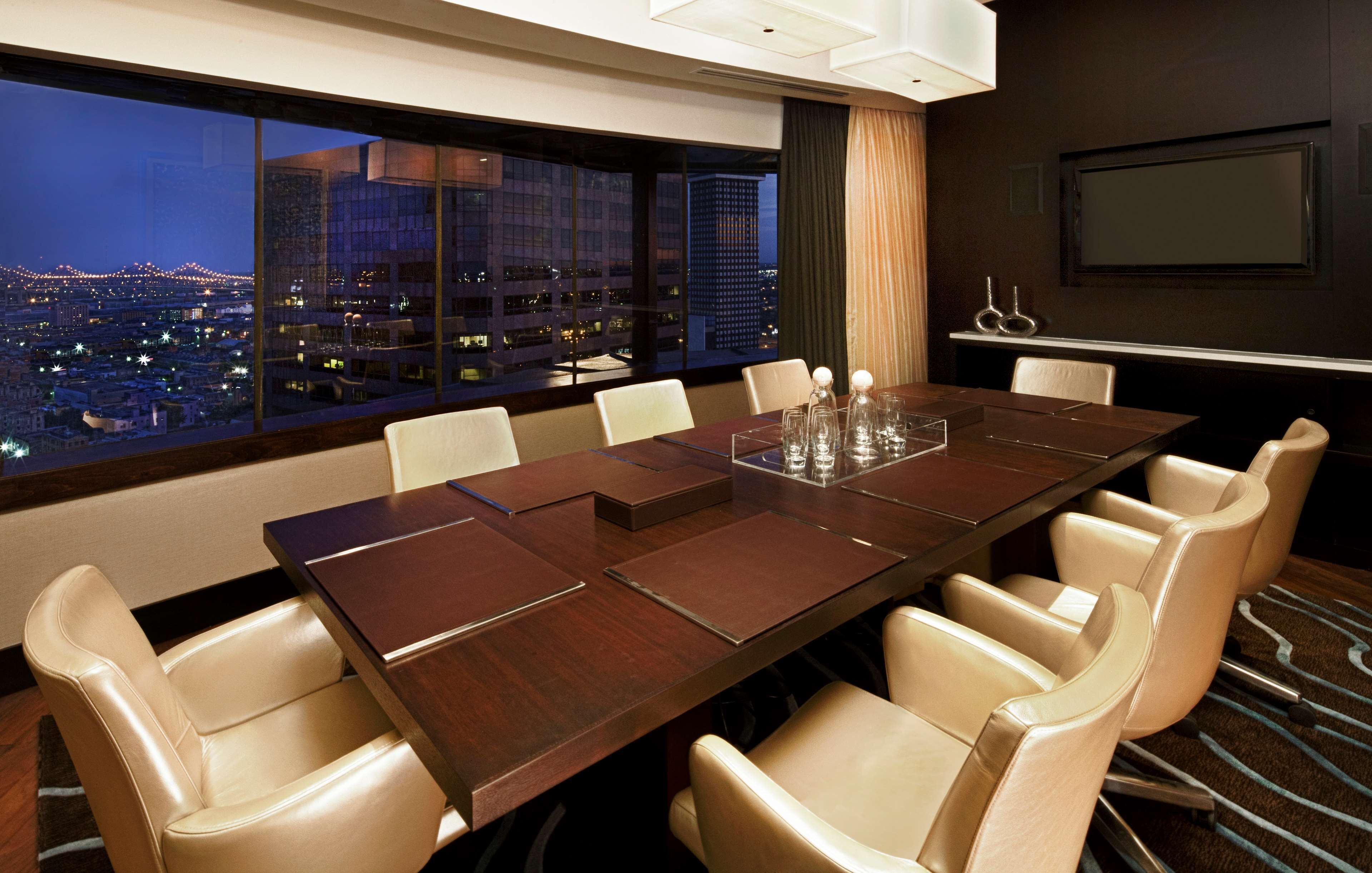 A conference room with a large table, beige chairs, a city view, a flat-screen TV, and a decorative item on the wall.