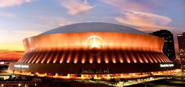 Un estadio grande y moderno con un llamativo logotipo de Mercedes-Benz en la fachada, rodeado de edificios urbanos.