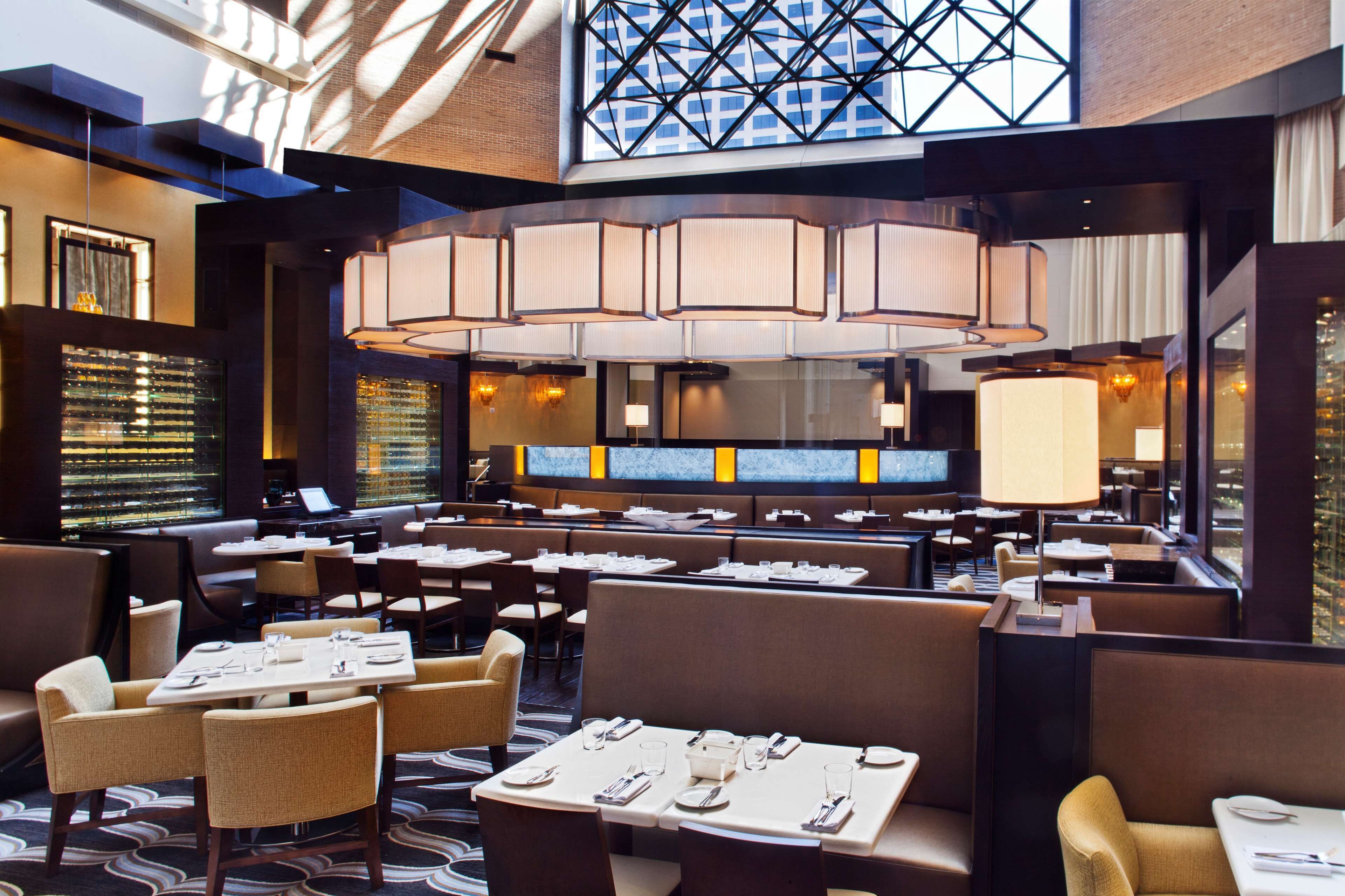 A modern restaurant with high ceilings, large windows, and a variety of seating arrangements including booths and tables.