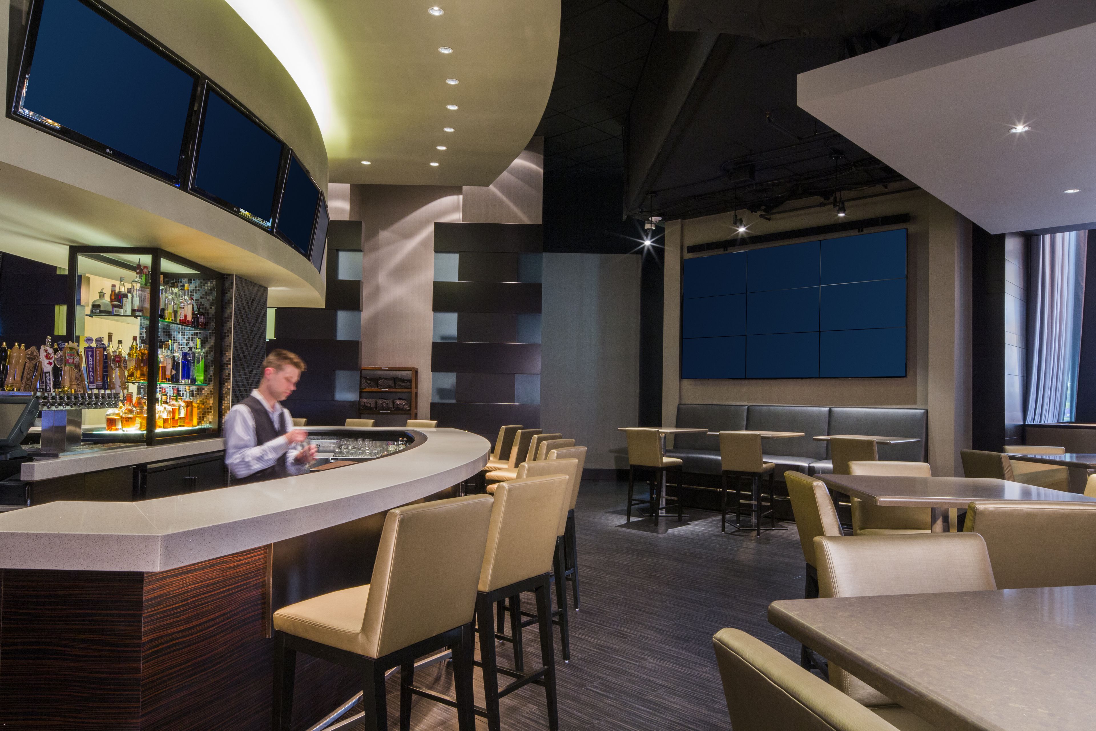 Un espace bar moderne avec un barman, des tables et des chaises, et un grand écran.