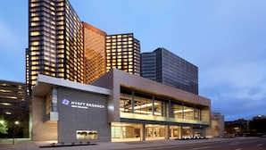 A modern Hyatt Regency hotel with a prominent glass facade, located in a cityscape with high-rise buildings.