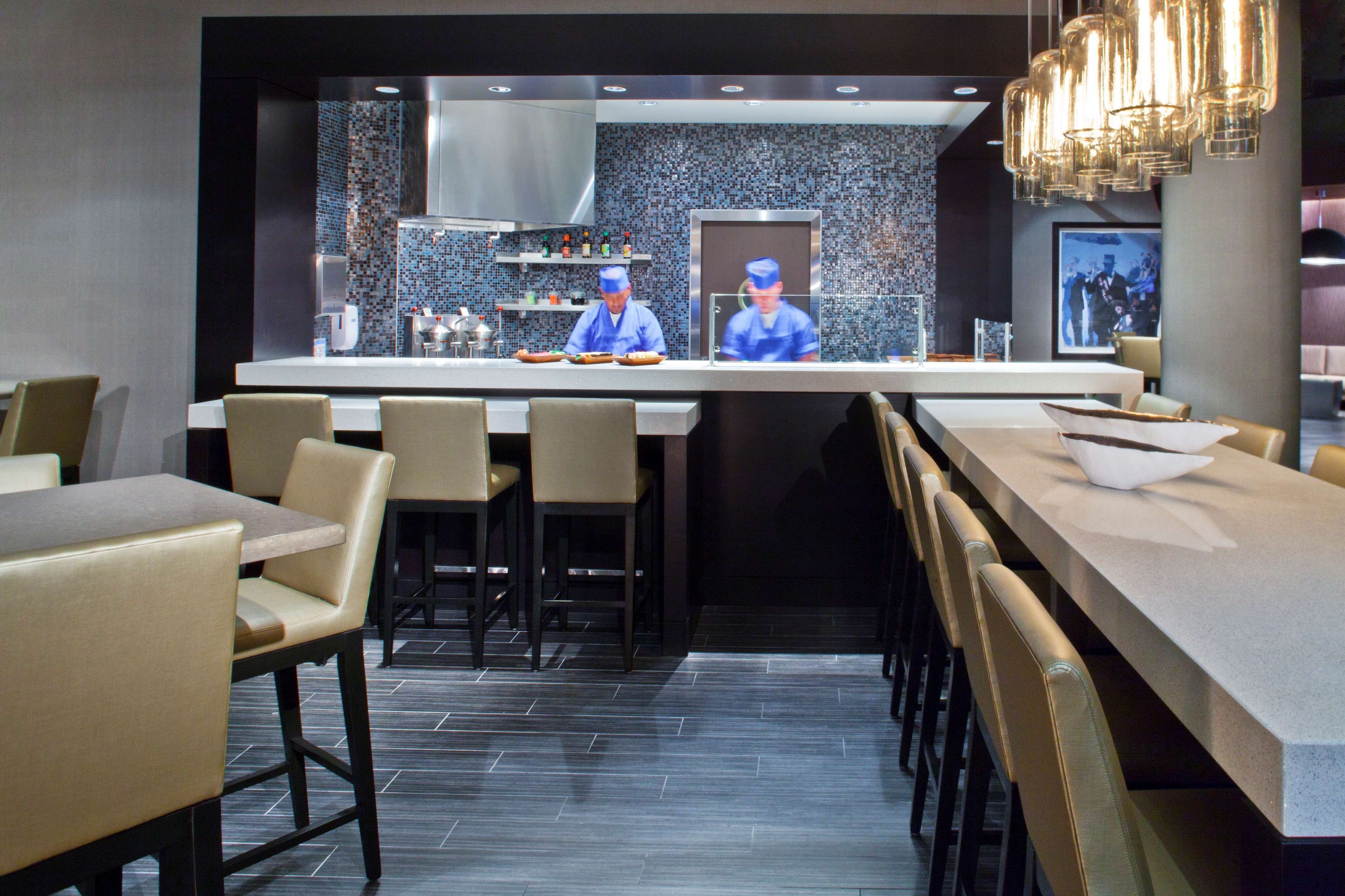 Um restaurante moderno com área de bar central, assentos em ambos os lados e backsplash de azulejos na cozinha.
