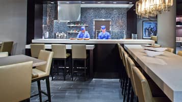 Um restaurante moderno com área de bar central, assentos em ambos os lados e backsplash de azulejos na cozinha.