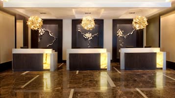 A reception area with three reception desks, each with a unique chandelier and wall art. The floor is polished marble, and the ceiling has recessed lighting.