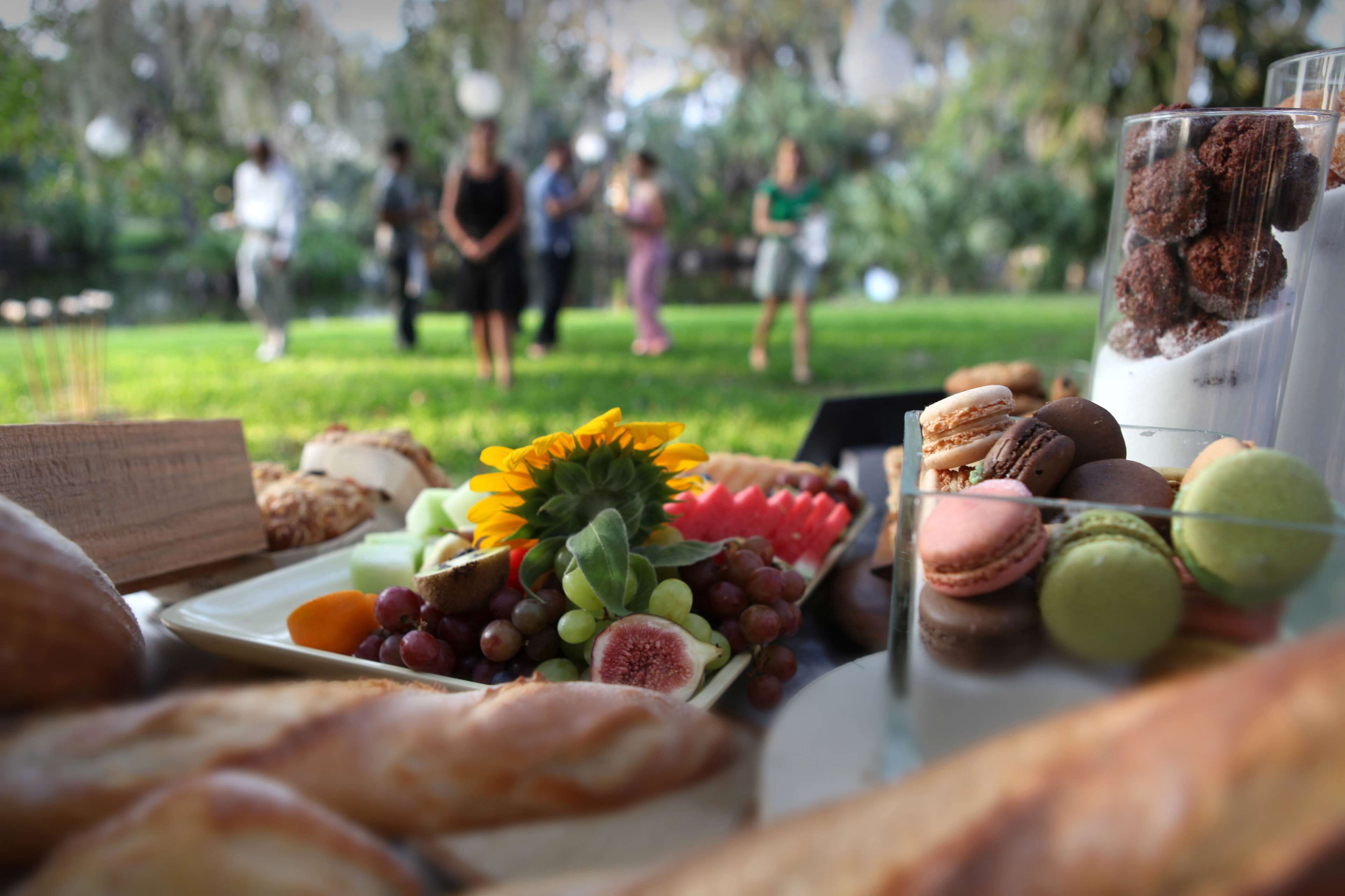 An outdoor buffet with various food items and a group of people in the background.