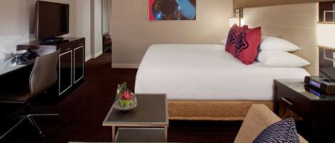 A hotel room with a bed, a desk with a computer, a TV, and a small table with a decorative item.