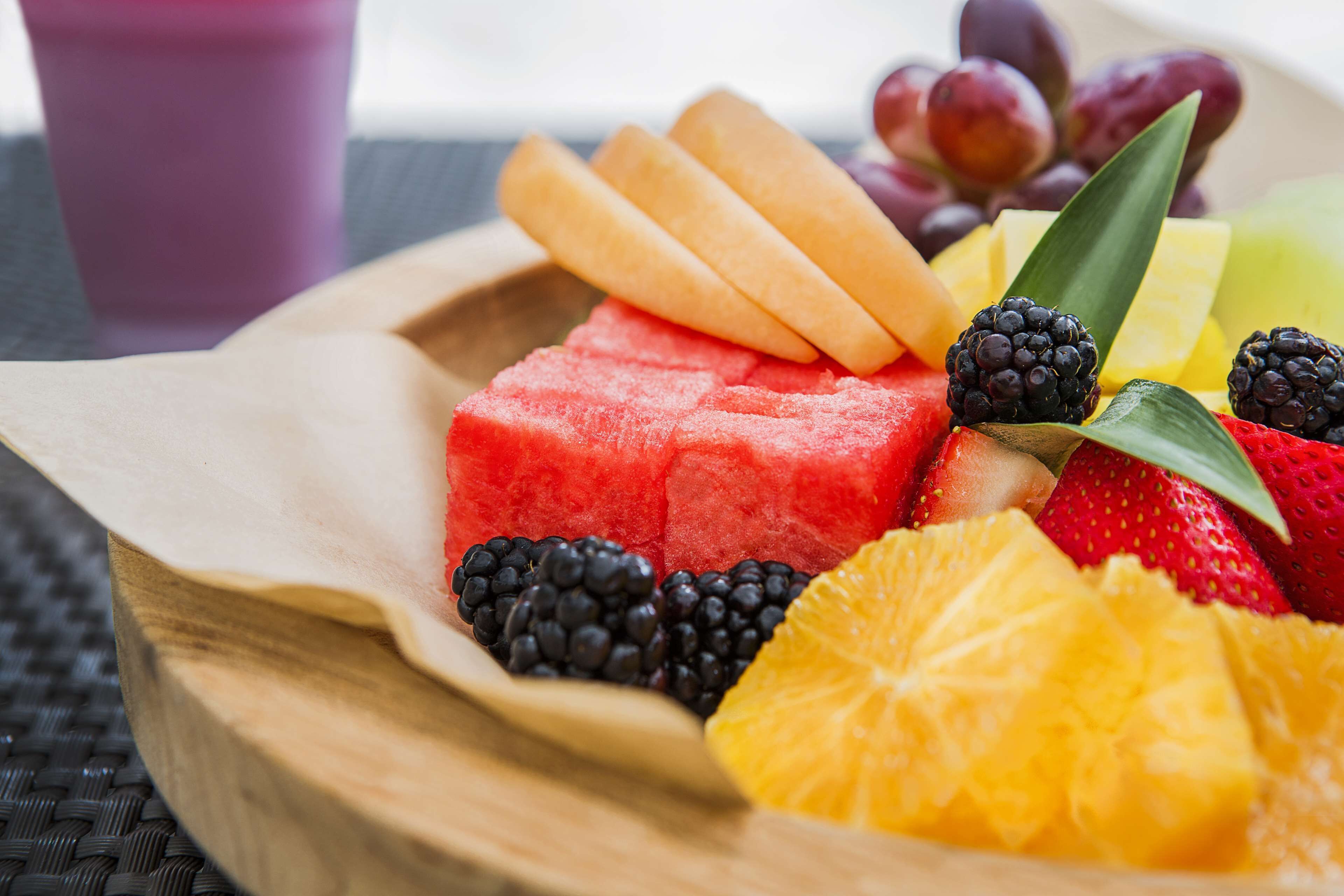 A wooden tray with various fruits including watermelon, strawberries, blackberries, and pineapple slices.