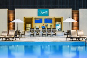 Un  área de piscina con un bar llamado 'Bywater Pool Deck & Bar', que cuenta con sillones de descanso y sombrillas.
