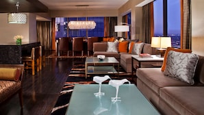 A modern hotel lobby with a sofa, chairs, a dining area, and a view of the city at night.