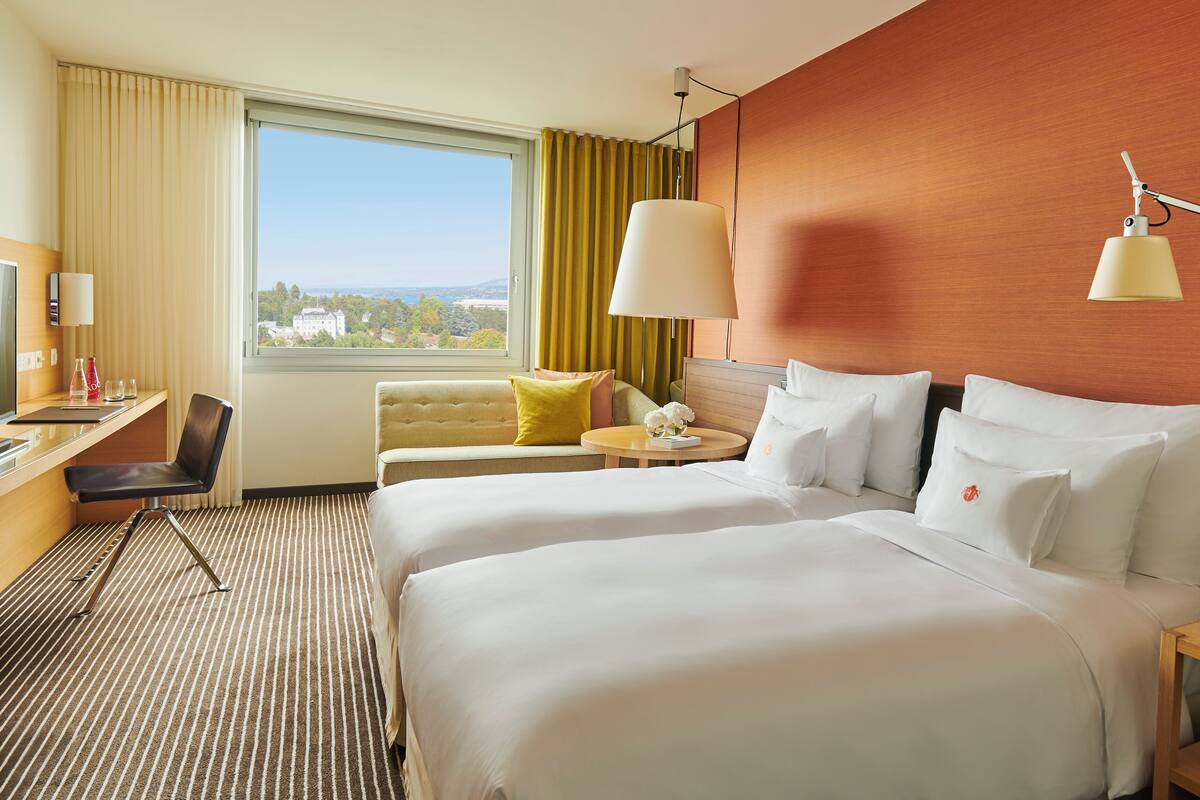 A hotel room with a large bed, a desk, a chair, and a view of the outdoors.