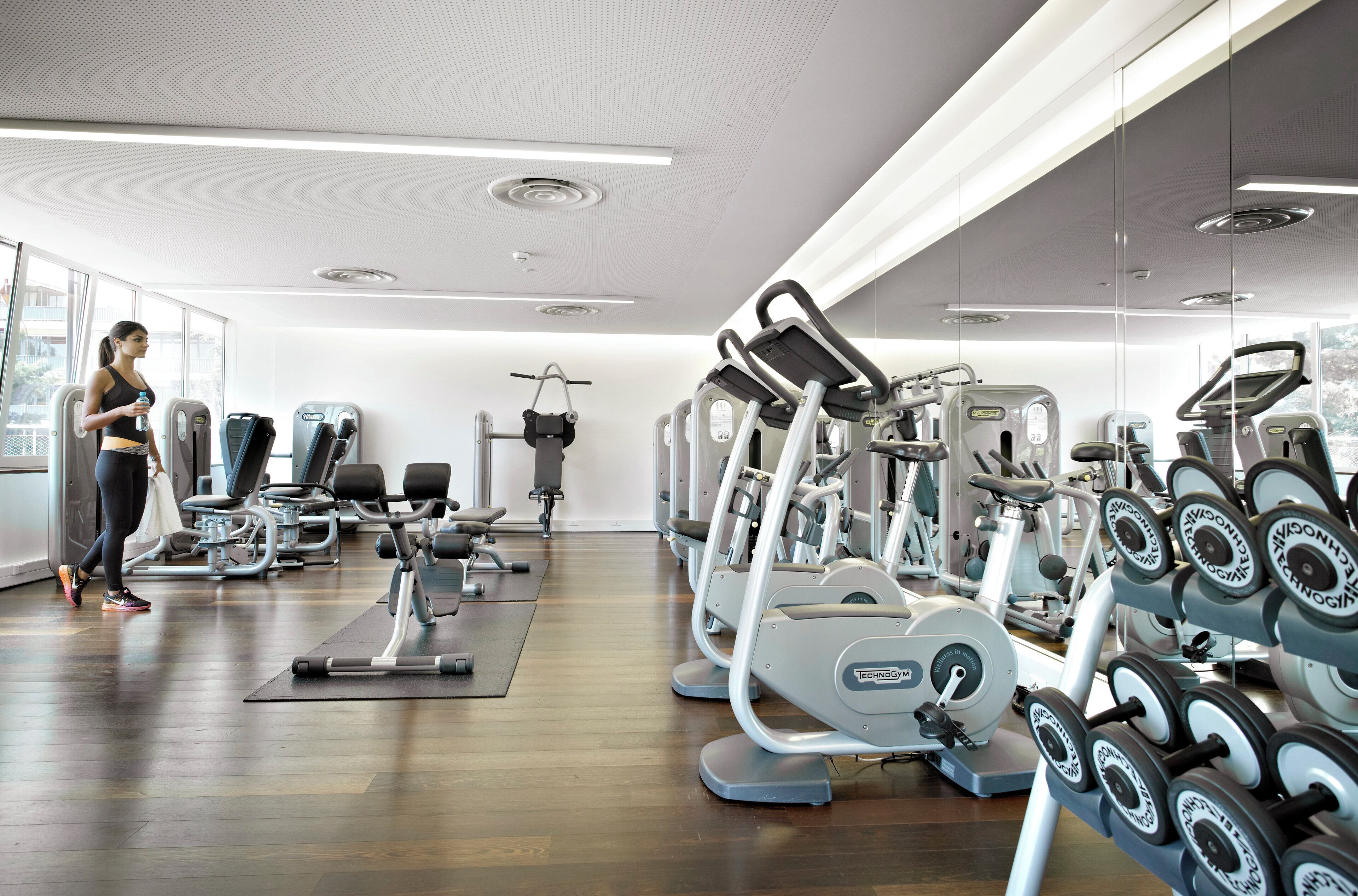 Un gimnasio con diversos equipos de ejercicio, incluyendo cintas de correr y máquinas de pesas, y una persona haciendo ejercicio.