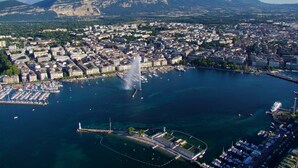 An aerial view of a coastal city with a marina, buildings, and a mountain in the background.