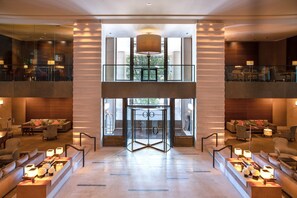 A spacious lobby with a double-height ceiling, a glass elevator, and seating areas with tables and chairs. - InterContinental Geneve by IHG (Geneva)