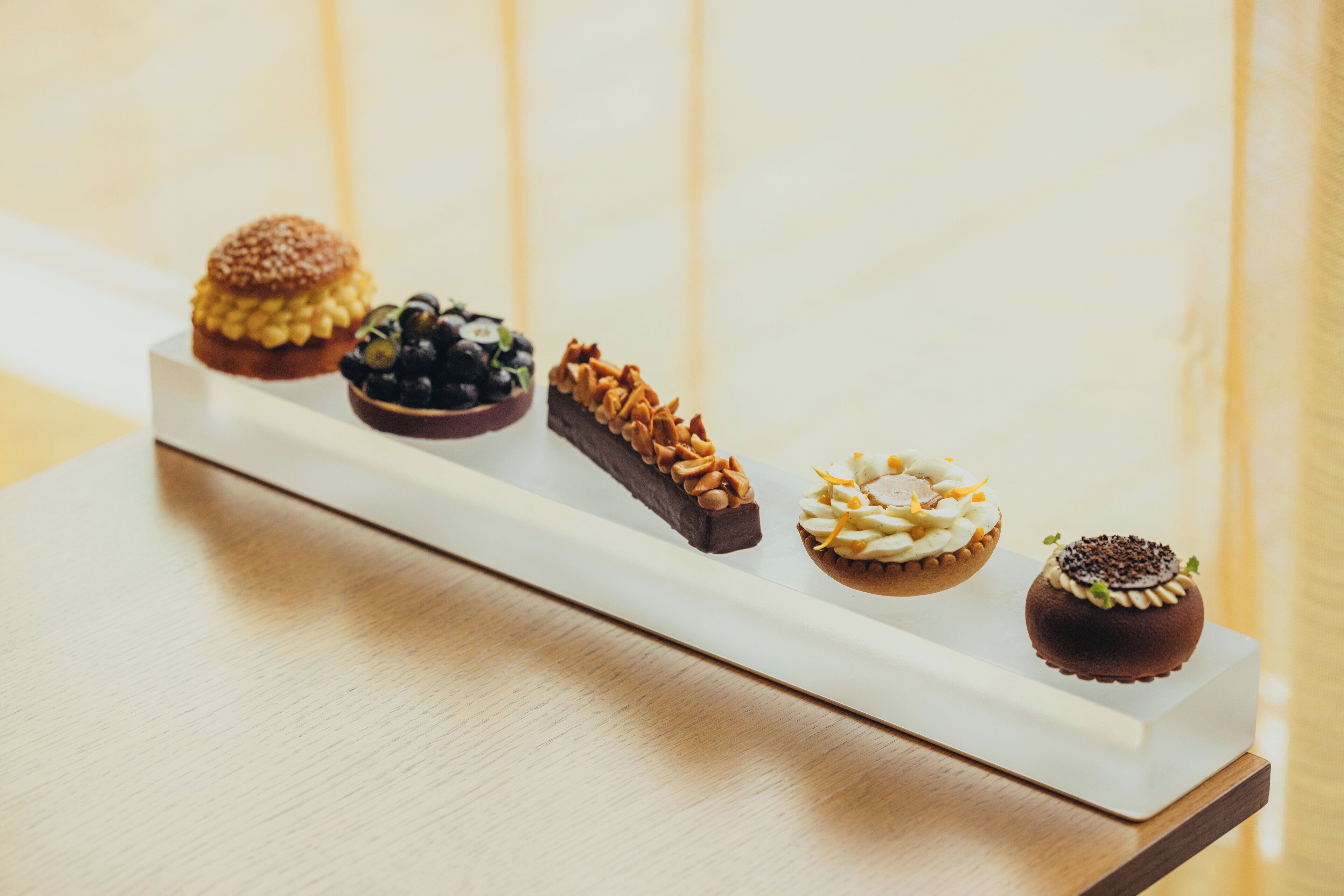 Un plateau rectangulaire blanc contenant cinq desserts différents, posé sur une surface en bois.