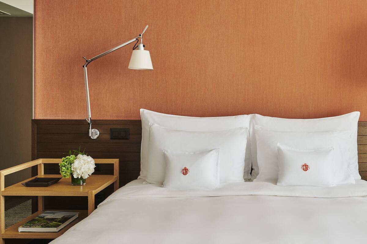 A neatly made bed with white linens, two bedside tables with lamps, and a small round table with a vase of flowers.