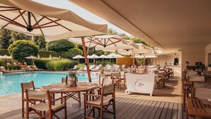 Zona junto a la piscina con sillones, sombrillas y un bar.