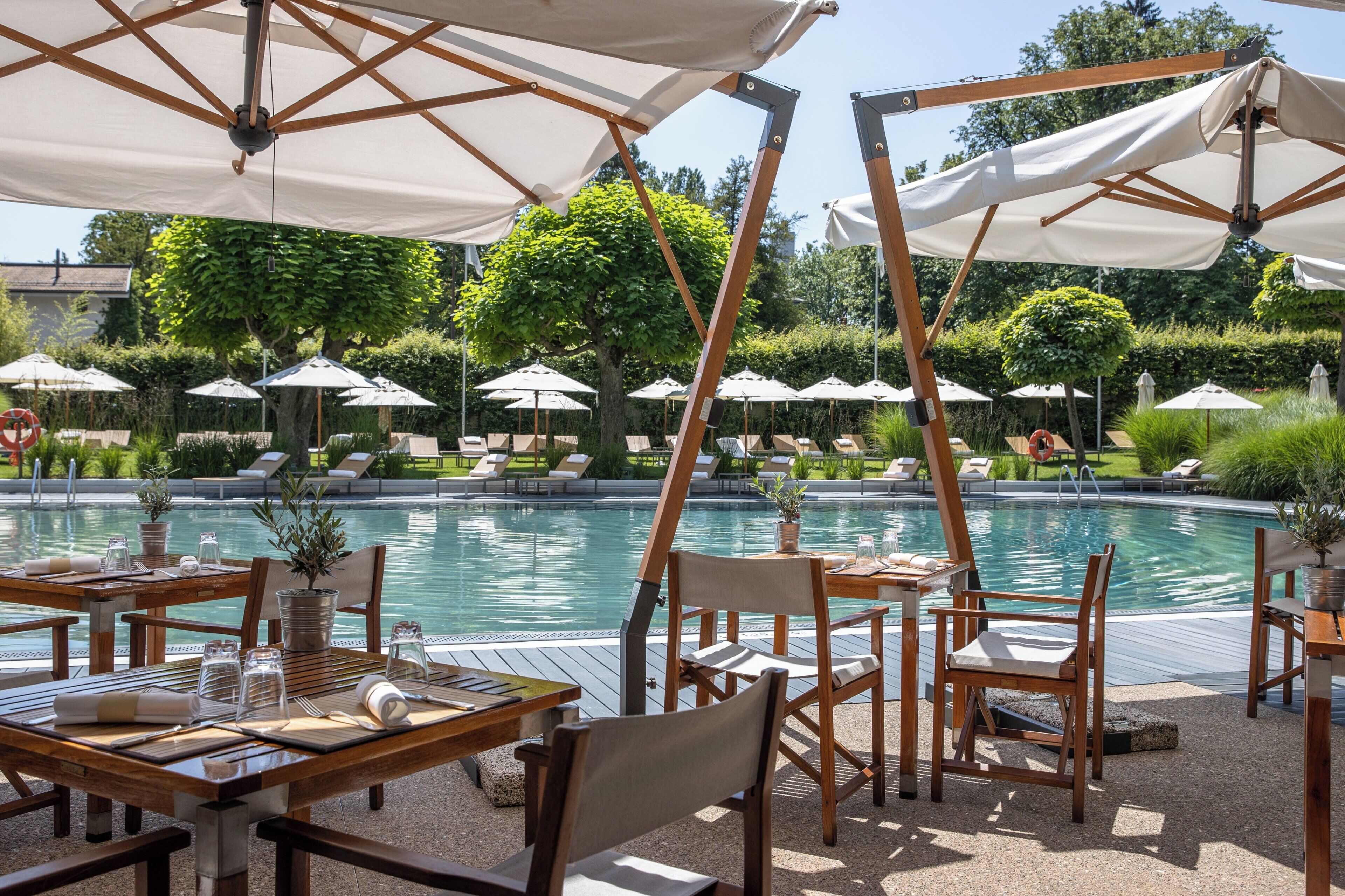 A poolside area with tables, chairs, and umbrellas.