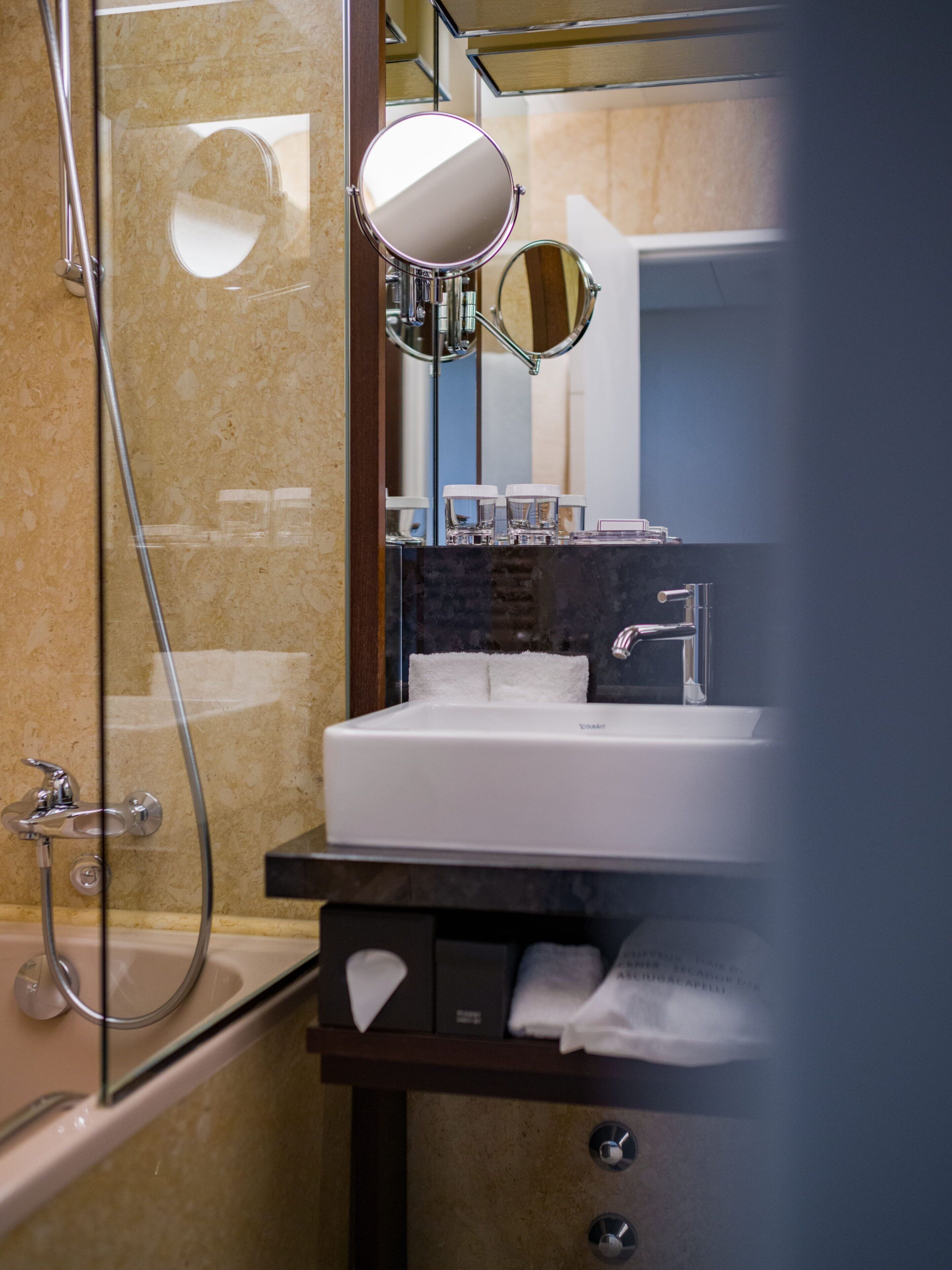 A bathroom with a glass shower enclosure, a sink with a mirror above it, and a towel rack.