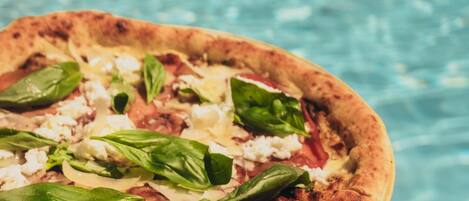 A pizza with various toppings held over a poolside area.