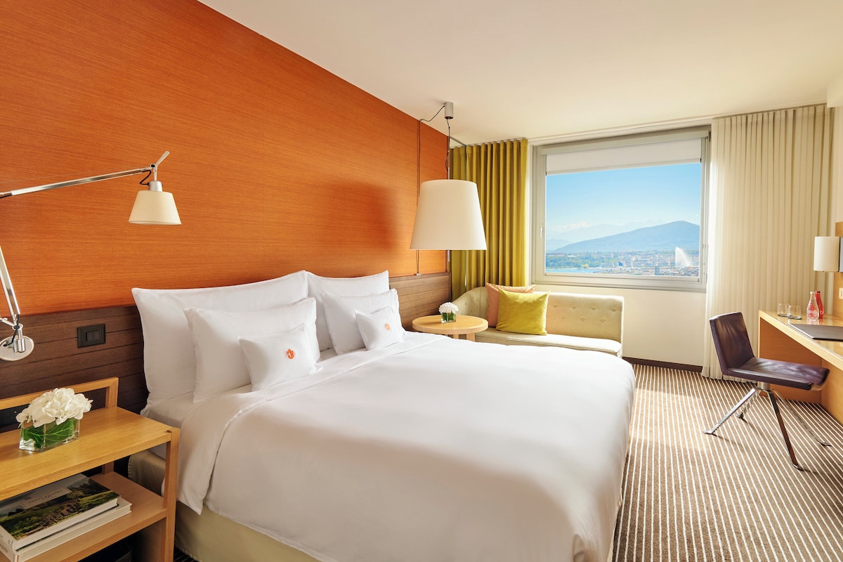 Habitación de hotel con una cama grande, un escritorio, una silla, una lámpara, una ventana con vistas y un televisor.