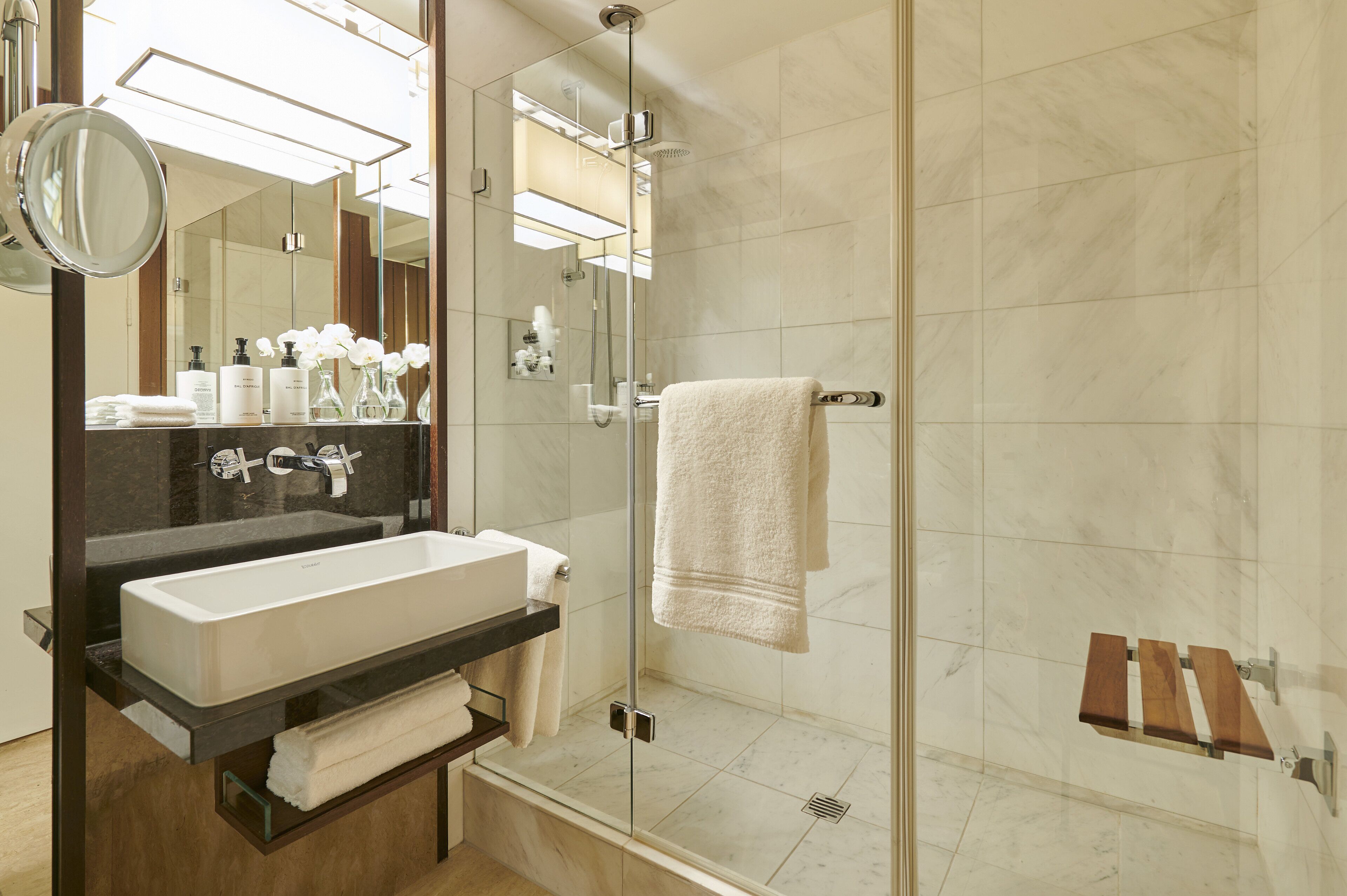 Un baño moderno con un espejo grande, un lavabo blanco y una ducha con paredes de vidrio.